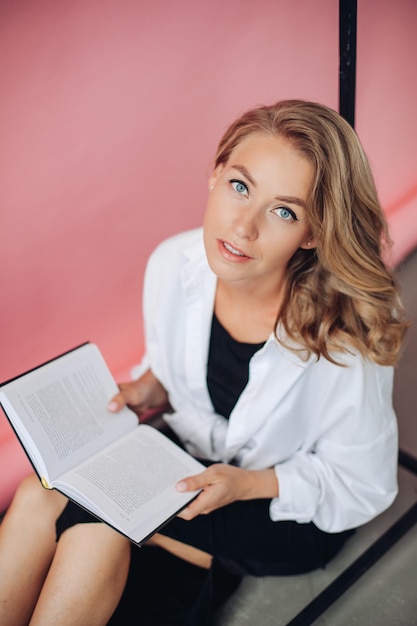 Hermosa mujer caucásica con cabello rubio sosteniendo un libro y mirando a la cámara