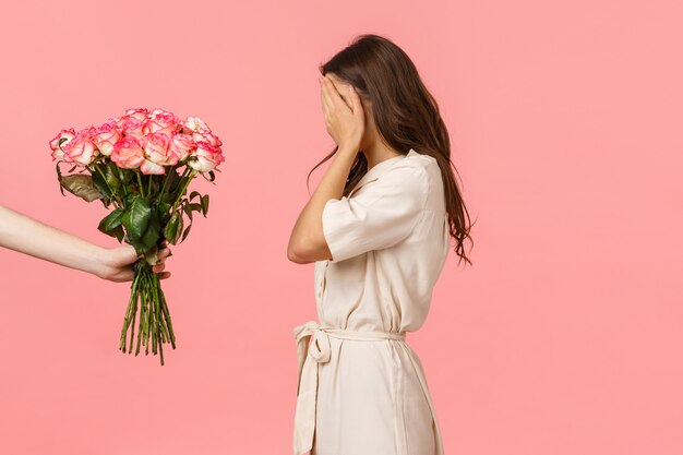 Hermosa mujer caucásica femenina en disfraces, ojos cerrados con las palmas de las manos como sorpresa que espera, mano que sostiene rosas ramo encantador, admirador secreto expresa afecto con regalo, rosa