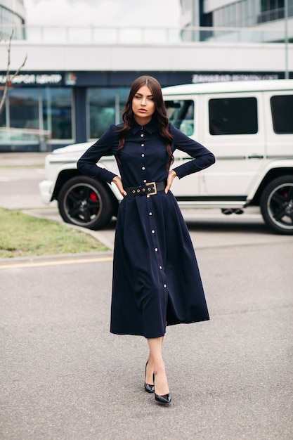 Hermosa mujer caucásica joven con cara bonita en un hermoso vestido negro con una longitud por debajo de la rodilla camina hacia la calle