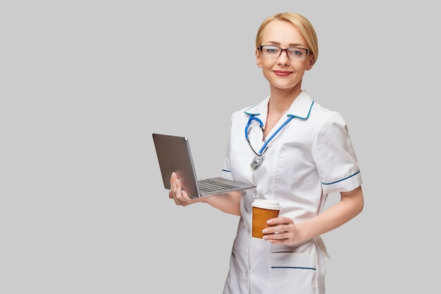 Hermosa mujer caucásica médico o enfermera sosteniendo una computadora portátil y una taza de café para llevar