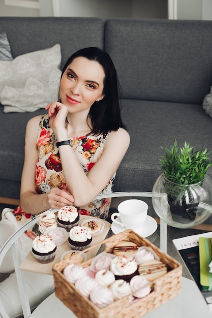 Hermosa mujer caucásica con pelo corto oscuro desayuna con dulces, malvaviscos y galletas