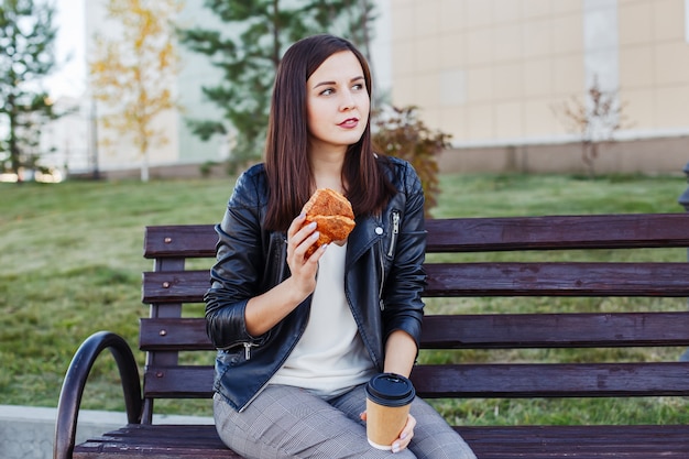 Hermosa mujer caucásica sentado en el parque y comiendo croissant