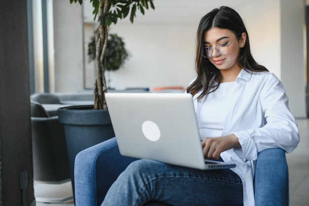 Hermosa mujer caucásica soñando con algo mientras se sienta con un netbook portátil en un moderno café bar, una joven y encantadora mujer independiente que piensa en nuevas ideas durante el trabajo en una computadora portátil