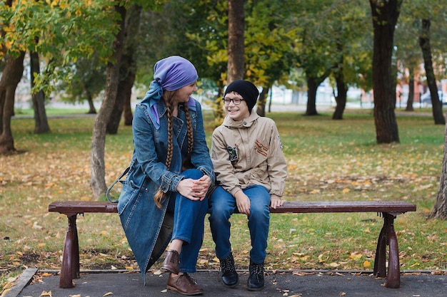 Hermosa mujer caucásica y su hijo sentados en el parque en un banco familia de otoño