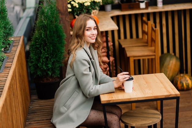 Hermosa mujer caucásica tomando café en la cafetería, sonriendo, hablando por teléfono