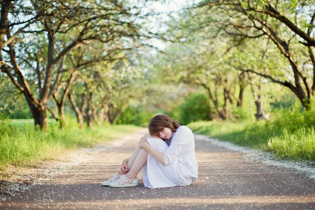 Hermosa mujer caucásica con vestido blanco camina en el jardín de flores de primavera