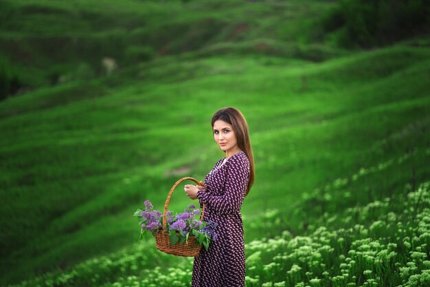 Hermosa mujer con una cesta de mimbre con flores en las colinas de fondo con flores.