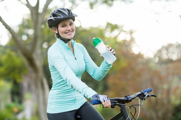 Hermosa mujer ciclista agua potable en bosque