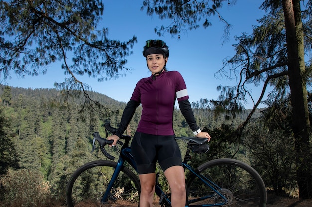 Hermosa mujer ciclista con gafas de sol y casco posando con su bicicleta en el bosque