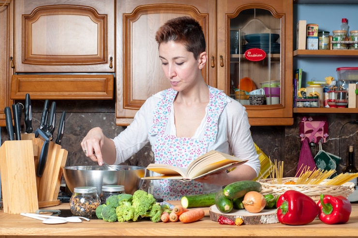 Foto hermosa mujer cocinando verduras con libro de cocina