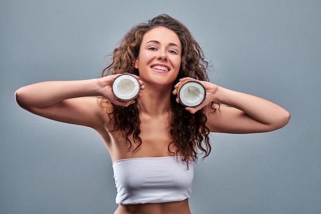 Hermosa mujer con coco en manos sobre fondo gris