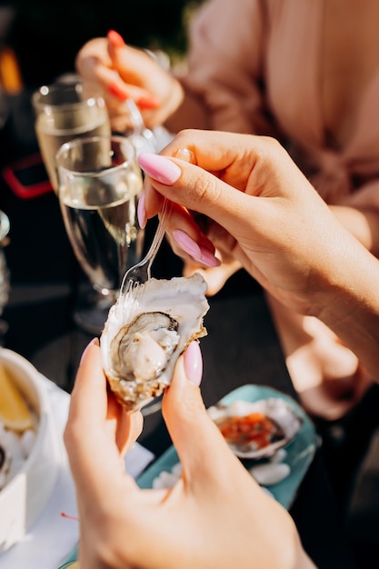 Foto hermosa mujer comiendo ostras frescas y bebiendo vino prosecco frío en el atardecer de verano en el restaurante delicias de mariscos