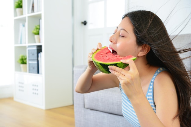 hermosa mujer comiendo sandía fresca y fría y disfrutando del viento fresco en casa para eliminar el calor del verano.