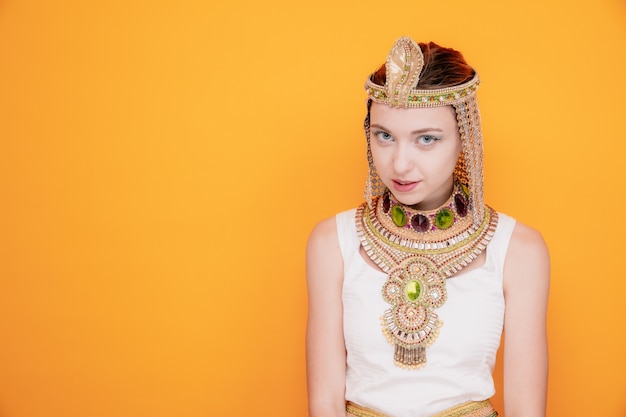 Foto hermosa mujer como cleopatra en traje egipcio antiguo mirando coqueteando sonriendo astutamente en naranja