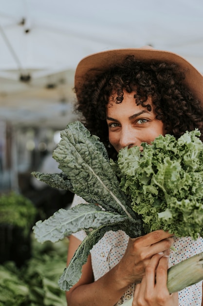 Hermosa mujer comprando col rizada en un mercado de agricultores