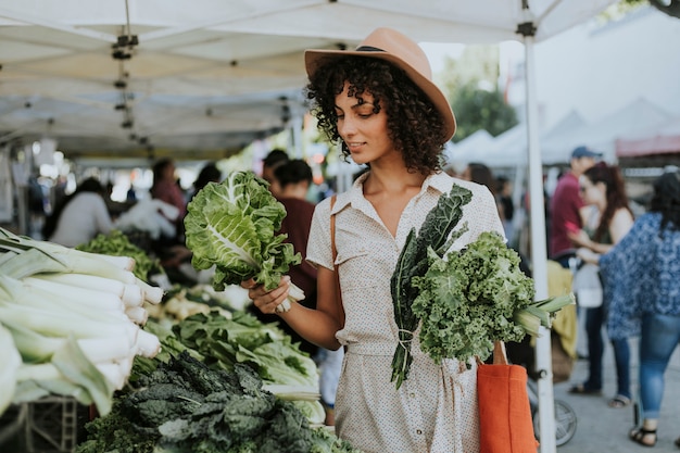 Hermosa mujer comprando col rizada en un mercado de agricultores