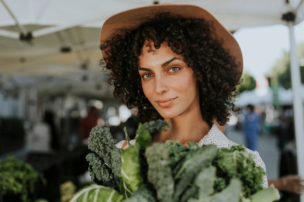 Hermosa mujer comprando col rizada en un mercado de agricultores