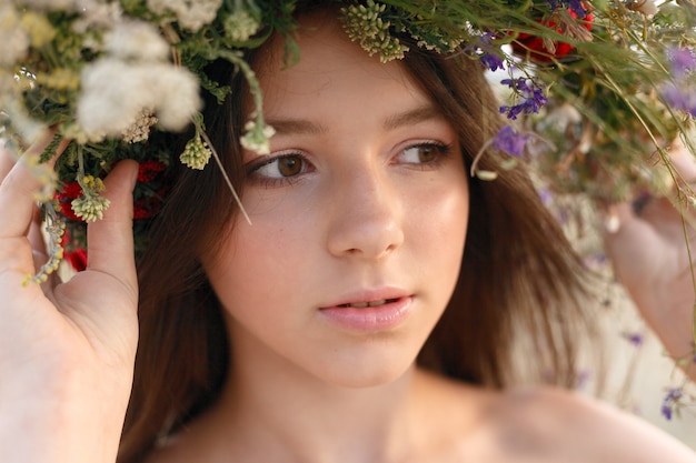 Hermosa mujer con una corona en la cabeza sentada en un campo de flores.