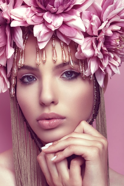 Hermosa mujer con corona de flores y maquillaje de la mano debajo de la barbilla