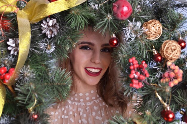 Hermosa mujer con corona de Navidad en manos sobre fondo azul.