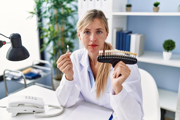 Hermosa mujer dentista comparando el blanqueamiento dental relajado con expresión seria en la cara. mirada simple y natural a la cámara.