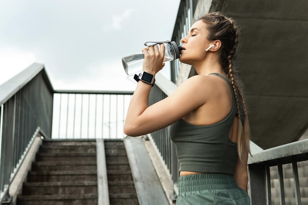 Hermosa mujer deportiva con una botella de agua después de hacer ejercicio o trotar en una calle de la ciudad