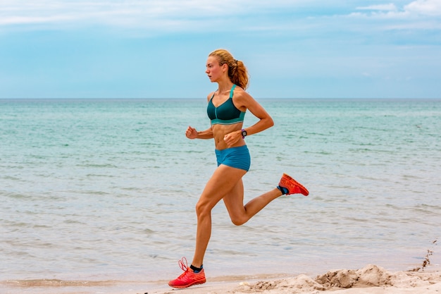 Hermosa mujer deportiva corriendo a lo largo de la hermosa playa de arena, estilo de vida saludable, disfrutando de unas activas vacaciones de verano cerca del mar