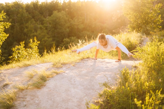 Hermosa mujer deportiva realizando pose de luciérnaga Señora haciendo ejercicios de yoga avanzados apoyándose en las manos en la noche exterior en el fondo de la luz del sol Mujer practicando Tittibhasana Yoga Pose en la naturaleza