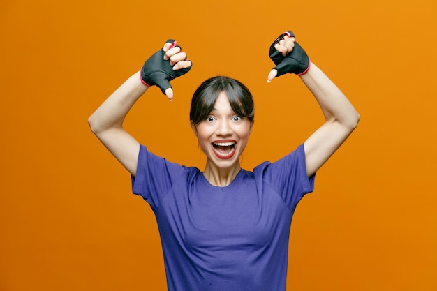 Hermosa mujer deportiva en ropa deportiva con guantes mirando a la cámara feliz y emocionada mostrando los pulgares hacia abajo de pie sobre fondo naranja