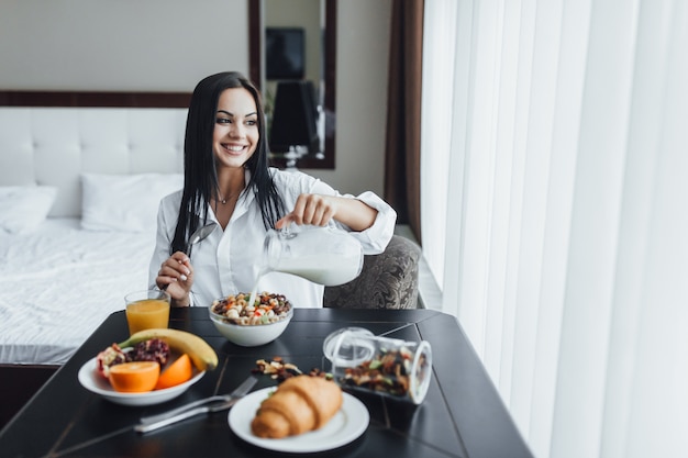 Hermosa mujer desayunando en la habitación del hotel. Ella sonríe y mira por la ventana