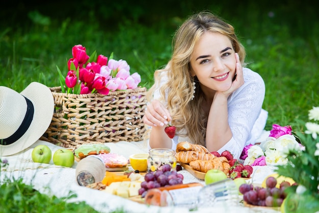 Hermosa mujer descansando en el parque sentado en una manta de picnic con frutas y vino