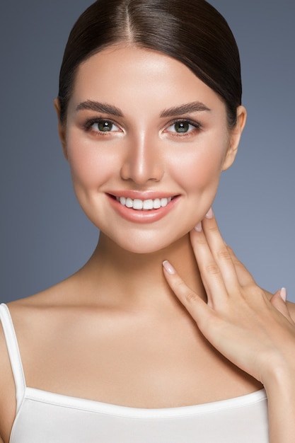 Hermosa mujer con dientes sanos sonrisa retrato de piel limpia y fresca. Sesión de estudio. Fondo gris.