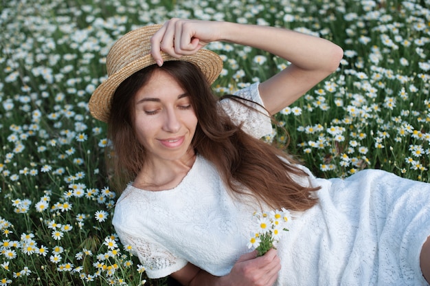 Hermosa mujer disfrutando del campo de manzanilla, bonita mujer acostada en el prado de flores, niña bonita
