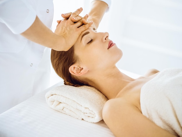 Hermosa mujer disfrutando de un masaje facial con los ojos cerrados en el centro de spa. Concepto de tratamiento de relajación en medicina.