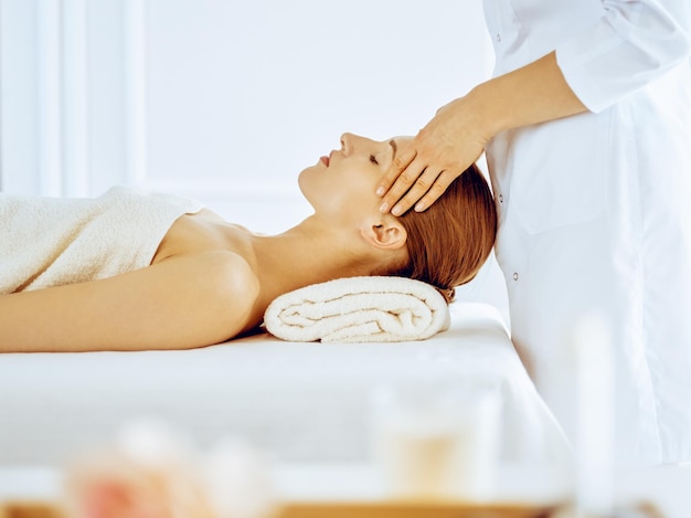 Hermosa mujer disfrutando de un masaje facial con los ojos cerrados en el centro de spa. Concepto de tratamiento relajante en medicina.