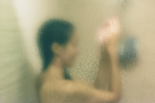Hermosa mujer en la ducha detrás de un vidrio con gotas