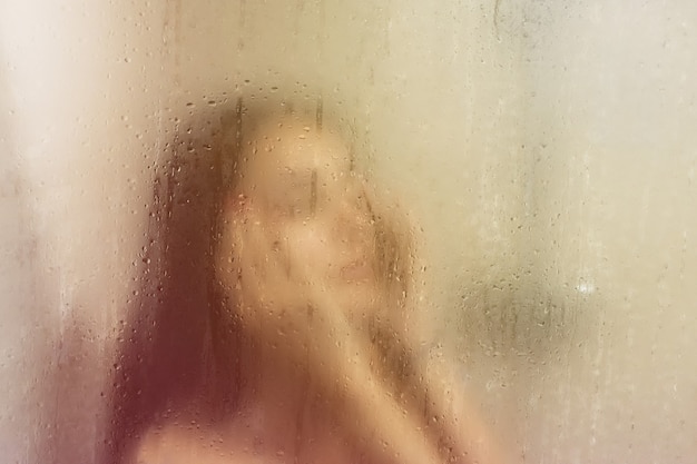 Hermosa mujer en la ducha detrás de un vidrio con gotas