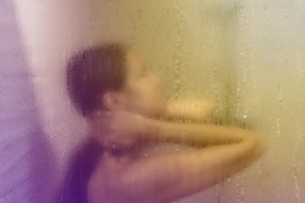 Hermosa mujer en la ducha detrás de un vidrio con gotas