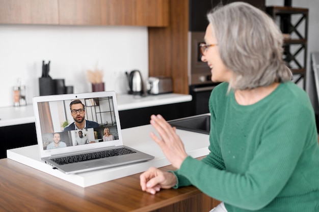 Una hermosa mujer de edad avanzada usando una computadora portátil para una reunión de video en casa