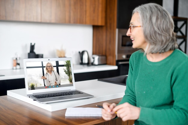 Una hermosa mujer de edad avanzada usando una computadora portátil para una reunión de video en casa