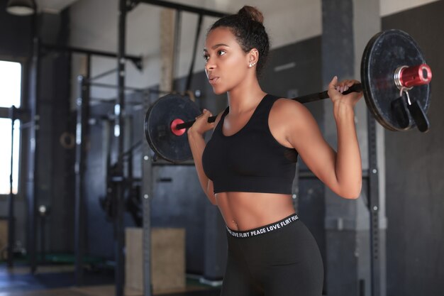 Hermosa mujer ejercicio en cuclillas con barra en el gimnasio.