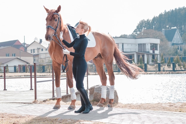 Hermosa mujer elegante caminando con un caballo en un club de campo. Deporte ecuestre, alquiler de caballos, concepto de ocio. Técnica mixta