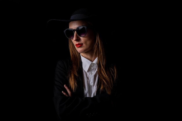 Hermosa mujer elegante de negocios con gafas de sombrero negro en un fondo negro
