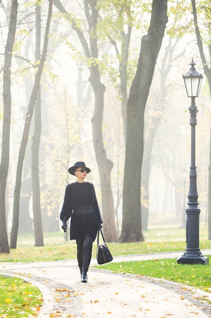 Hermosa mujer elegante con un sombrero negro en el parque otoño