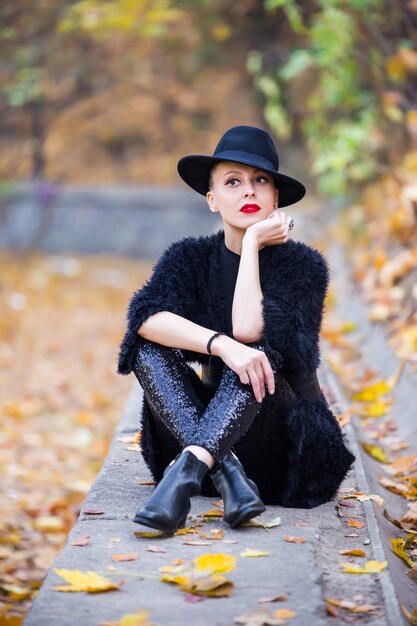 Hermosa mujer elegante con un sombrero negro en el parque otoño