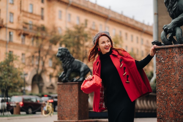 Una hermosa mujer elegante vestida con un elegante abrigo rojo con un elegante bolso rojo en la ciudad de otoño