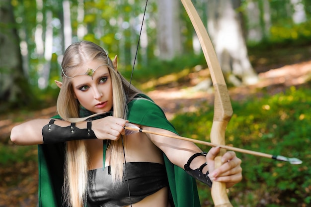 Hermosa mujer elfo arquero en el bosque cazando con un arco