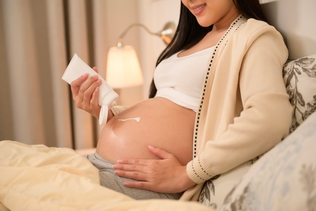 Una hermosa mujer embarazada aplicando crema hidratante para las estrías en el vientre
