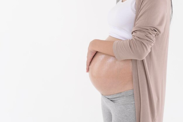 Una hermosa mujer embarazada aplicando crema hidratante para las estrías en el vientre