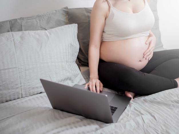 Hermosa mujer embarazada asiática está trabajando con su portátil